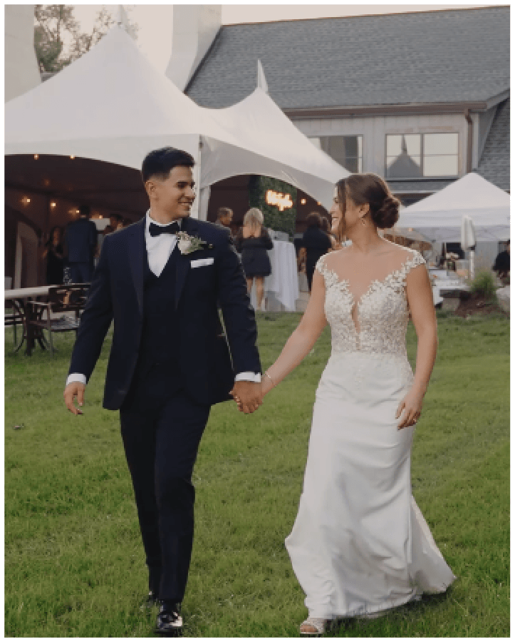 Newlywed couple walking hand in hand across a manicured lawn at an outdoor wedding reception