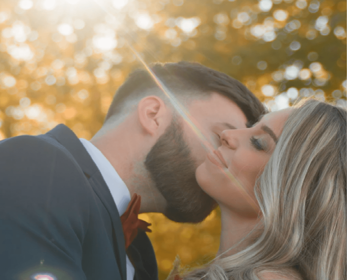 Couple sharing a kiss during golden hour with warm autumn foliage behind them