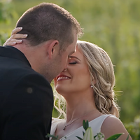A couple shares an intimate kiss outdoors against a soft green background during golden hour lighting.