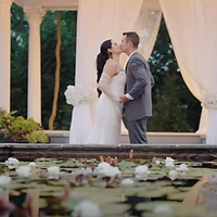 A bride and groom embrace beside a serene lily pond in an elegant garden venue during golden hour.