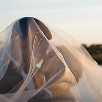 A person is wrapped in or adjusting a mosquito net during golden hour, creating a soft, ethereal composition with warm lighting.