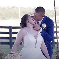 A bride and groom share a romantic moment outdoors at a ranch with a wooden fence visible in the background.