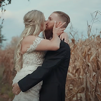 A newlywed couple shares a kiss in a golden hour setting amid a dried cornfield, capturing a romantic moment in their wedding day.