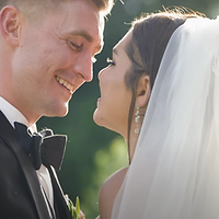 A bride and groom share an intimate kiss moment during their wedding ceremony, bathed in warm golden hour light with a soft green background.