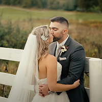 A bride and groom share a romantic kiss during their wedding ceremony in an outdoor rural setting during golden hour.