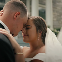 A bride and groom share an intimate kiss during their wedding ceremony in front of a classical stone building.