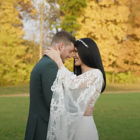 A bride and groom share a kiss during their wedding ceremony in front of a lush golden-green floral backdrop.