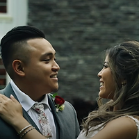 A close-up portrait of a couple in formal attire posing together against a brick wall, captured during daytime.