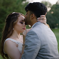 A couple shares an intimate moment outdoors during golden hour, with soft natural lighting and blurred green foliage in the background.