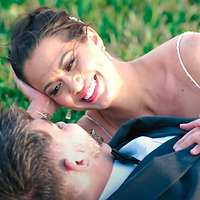 A close-up portrait of a couple embracing outdoors with a soft, blurred green background.