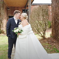 A bride and groom share a tender moment outdoors in front of a brick building on their wedding day.