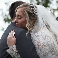A bride in an ornate white wedding dress and tiara embraces her groom in a tender, intimate moment during their wedding day.