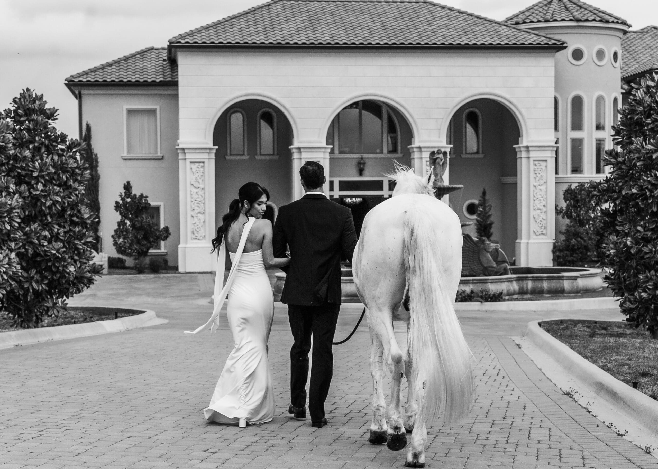 Bride and groom walk toward a classical white building with arched windows